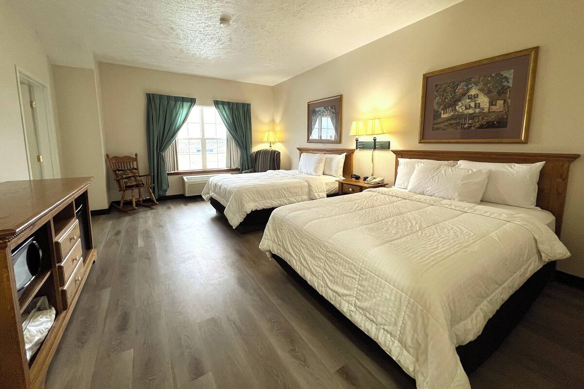 A hotel room with two beds, a desk, a chair, a lamp, and a painting on the wall.
