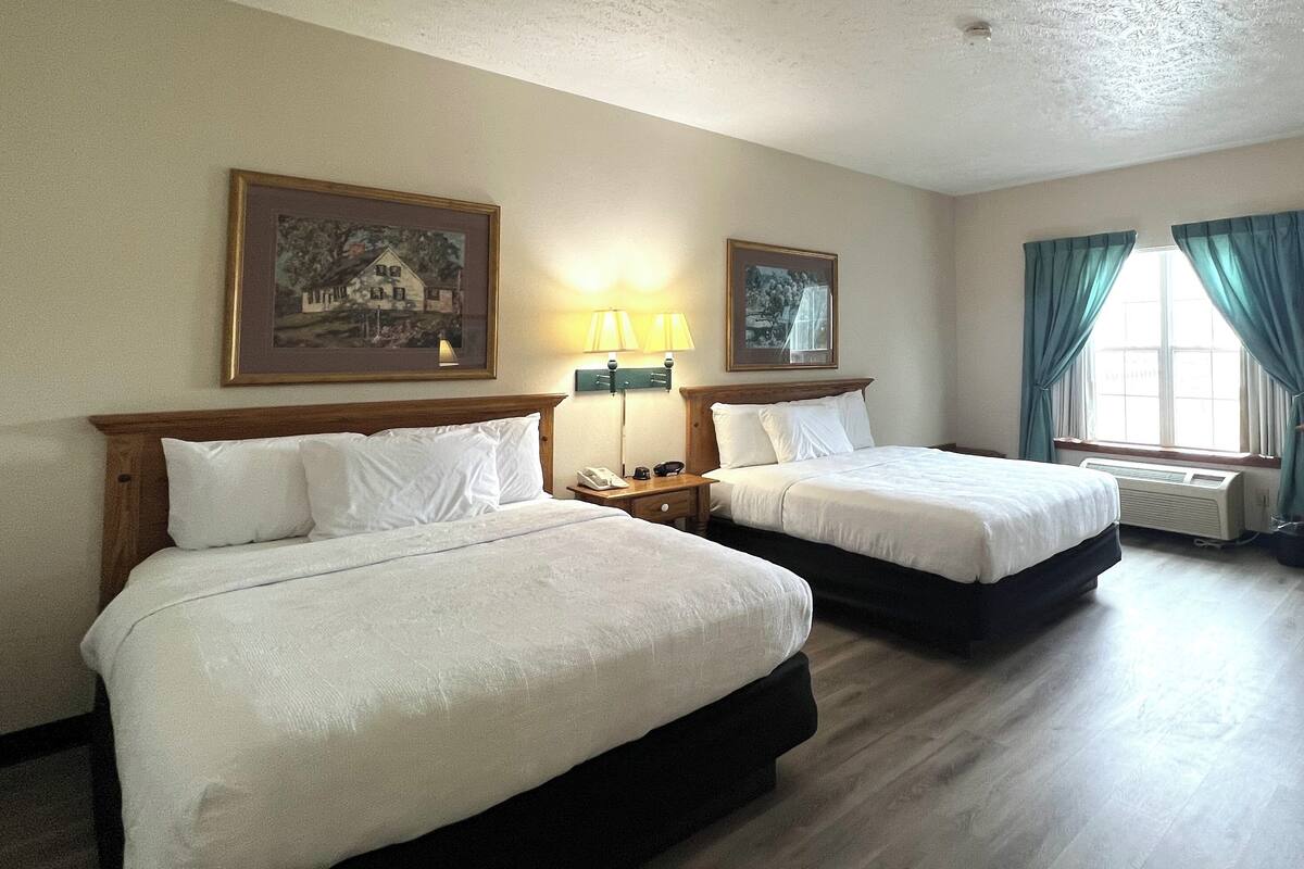A hotel room with two beds, a nightstand with a lamp, and two framed pictures on the wall.