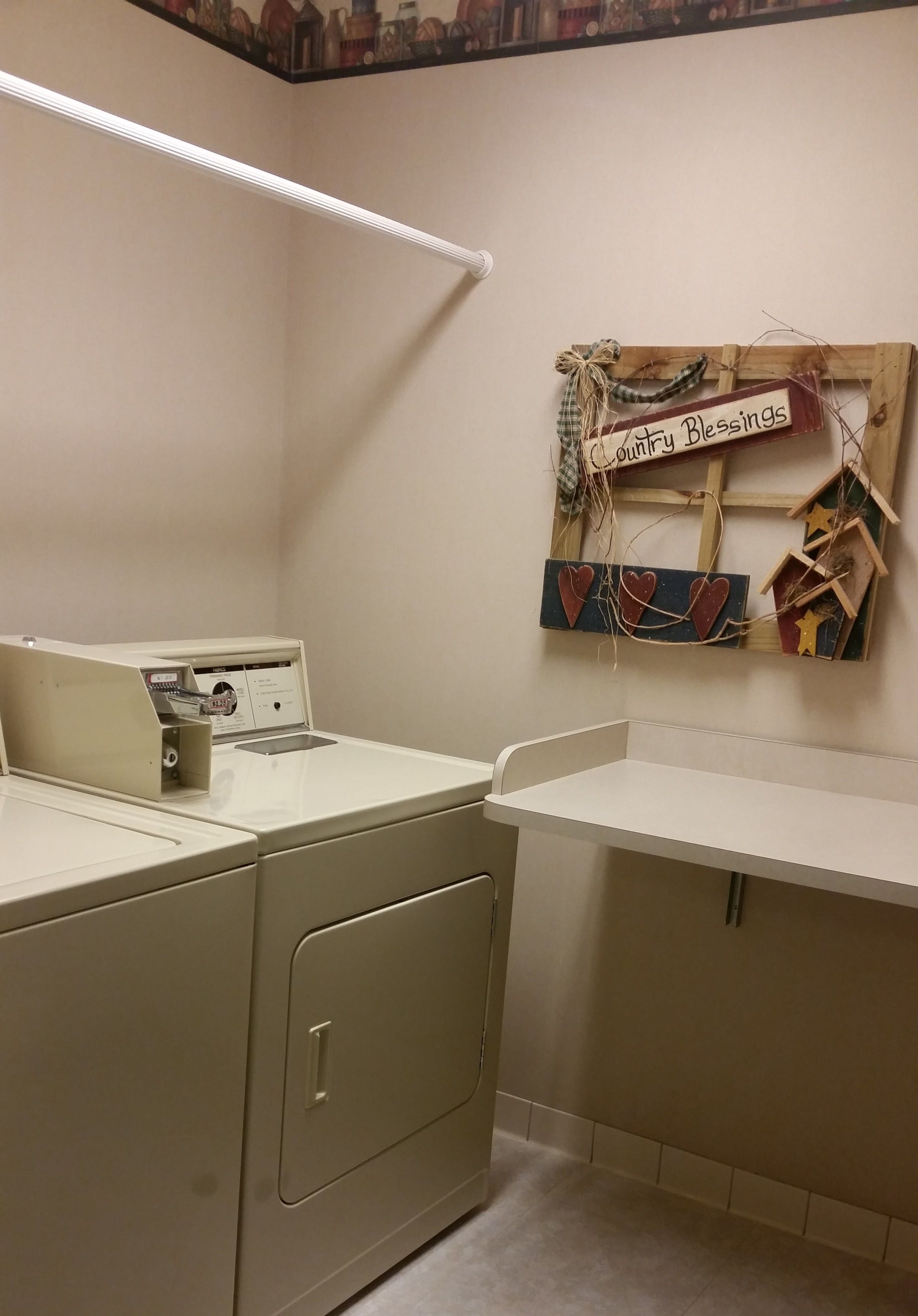 A laundry room with a washing machine, dryer, and a wall-mounted wooden sign that reads "Country Blessings."