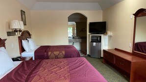 Une chambre d’hôtel avec deux lits, une télévision, un réfrigérateur et un miroir.