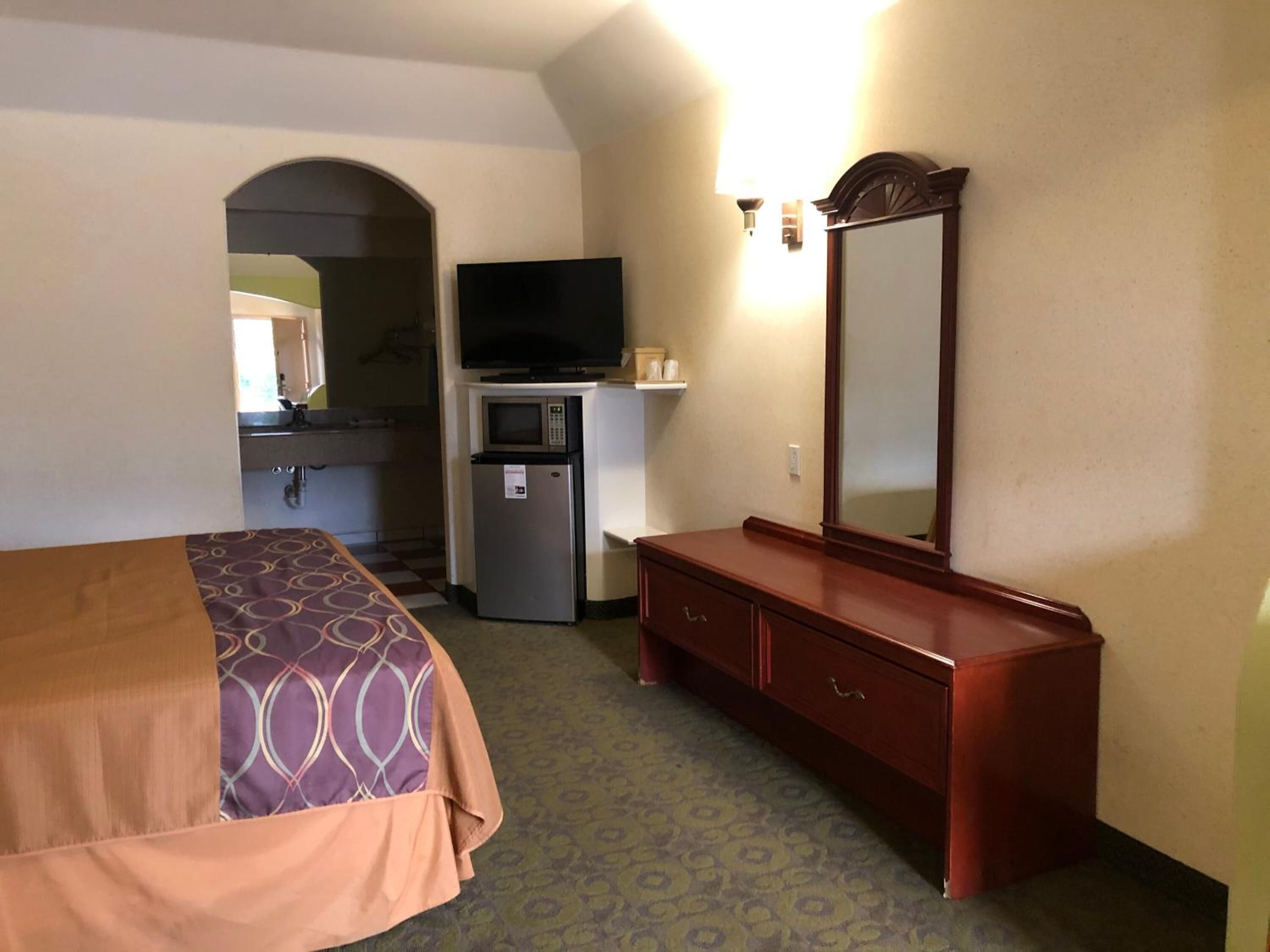 A hotel room with a bed, a small kitchenette, a television, a mirror, and a dresser.