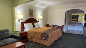 Une chambre d’hôtel comprenant un lit, un canapé, une petite table, un bureau, une lampe, un tableau accroché au mur et une salle de bain visible à travers une arche.