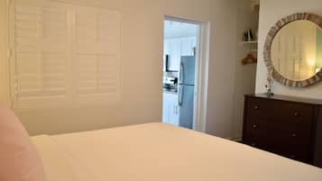 Un dormitorio con una cama, un aparador, un espejo y una puerta que da a una cocina.
