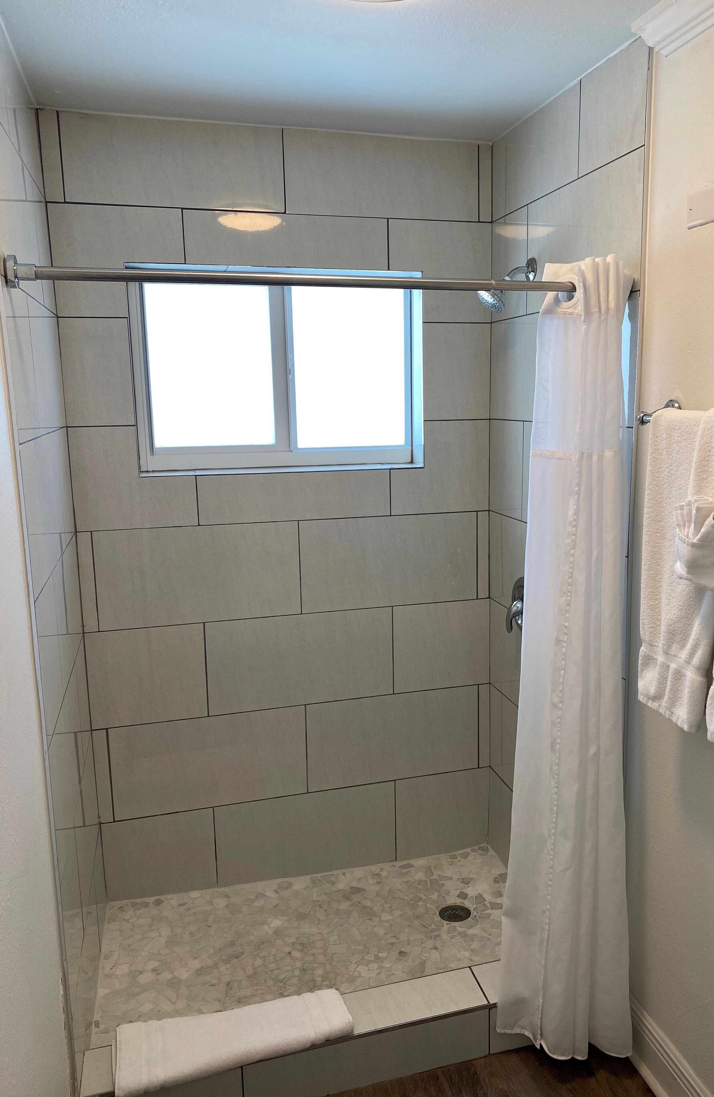 Ducha a pie con ventana, paredes enlosadas y cortina de baño.