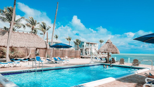 A pool area with lounge chairs, umbrellas, and a view of the ocean.