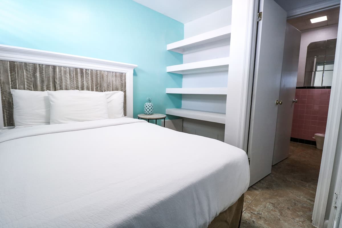 A hotel room with a bed, a small round table, and a white door leading to a bathroom.