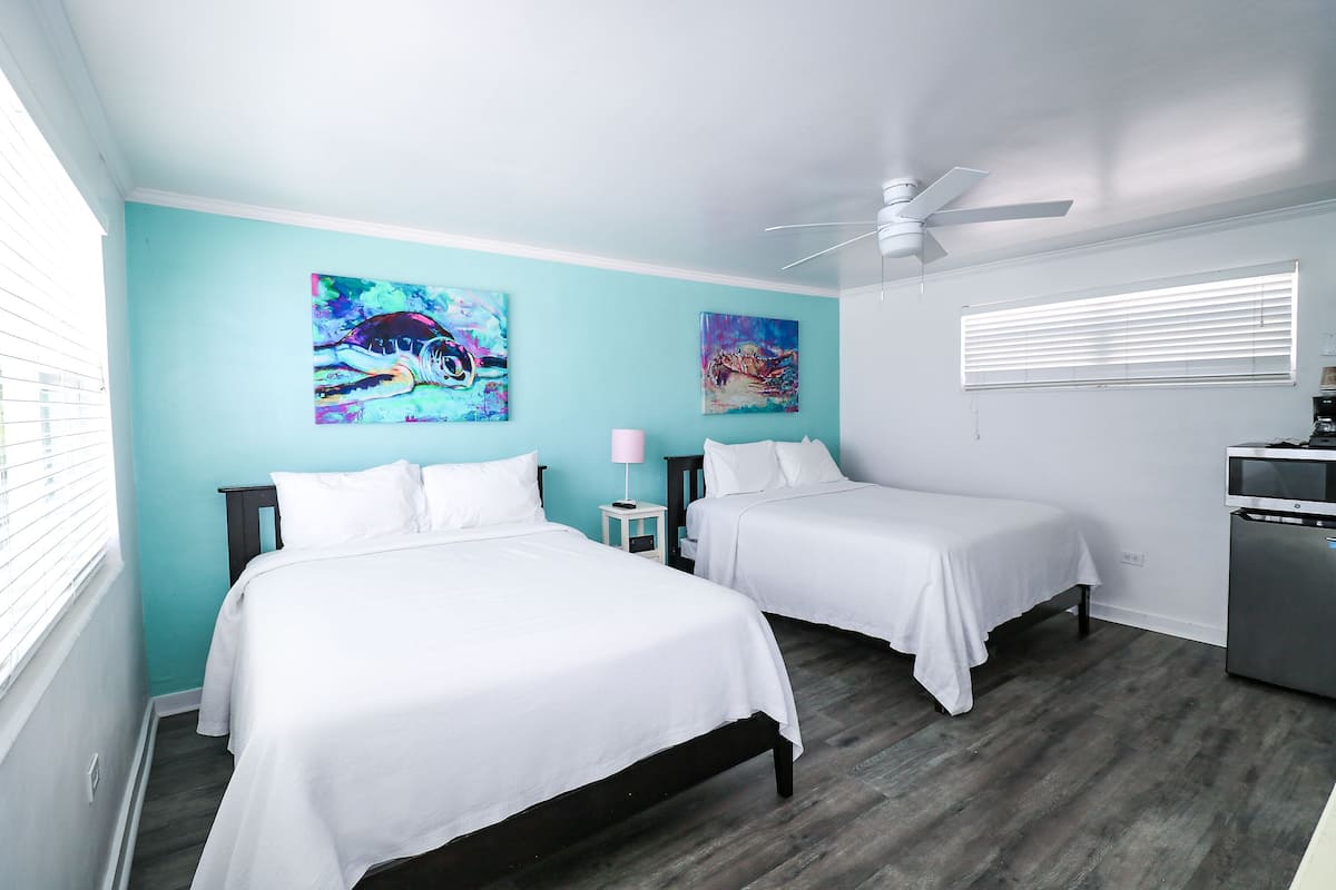 A room with two beds, teal walls, and artwork.
