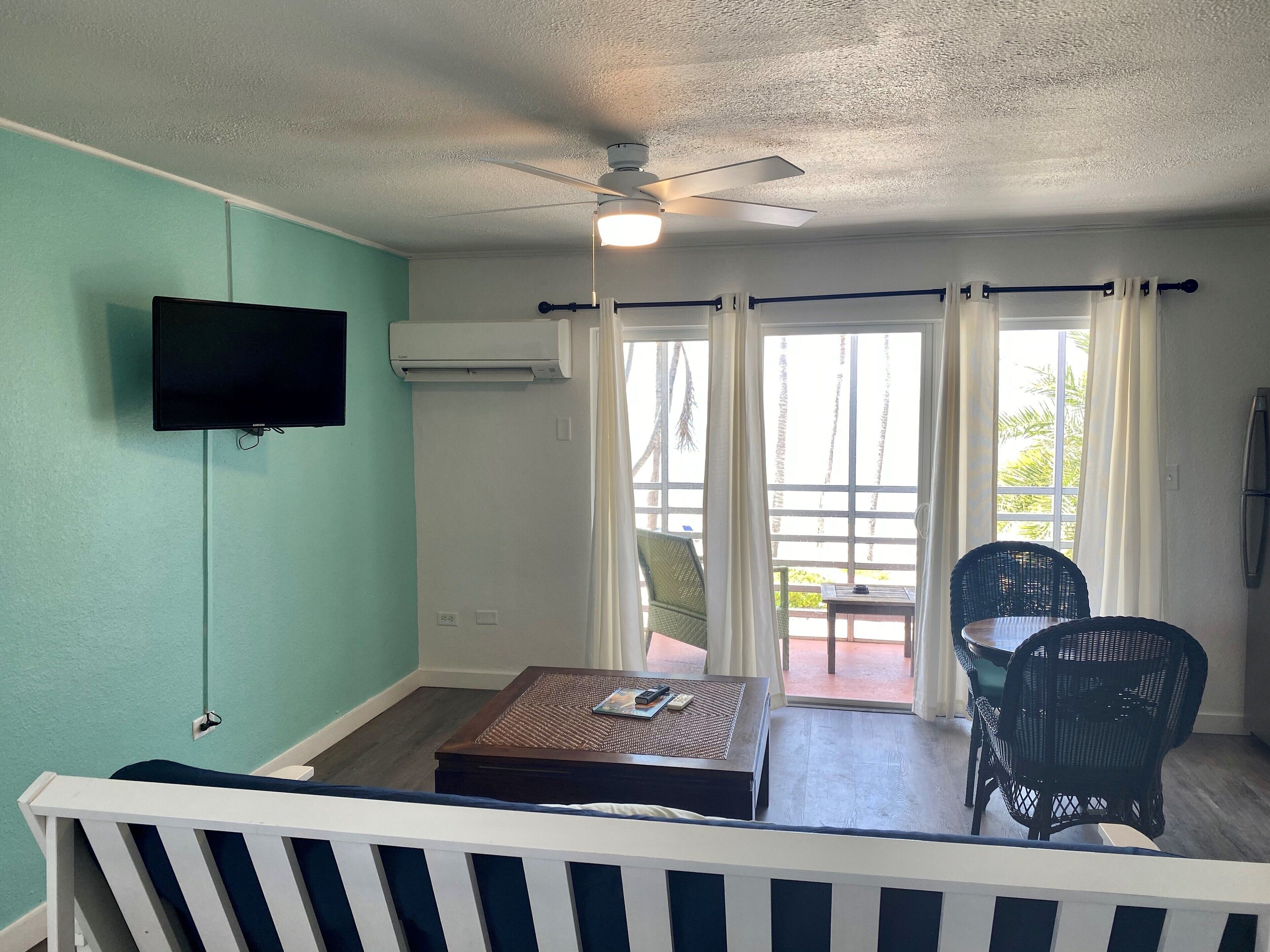 A room with a ceiling fan, a flat-screen TV, a small table with a mat, two wicker chairs, and a sliding glass door leading to an outdoor area.