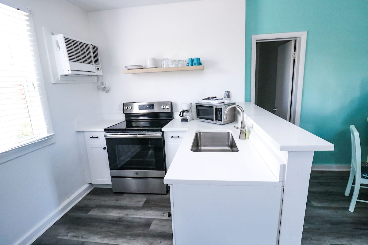 A modern kitchen with white cabinetry, a stainless steel oven, a microwave, and a white countertop.
