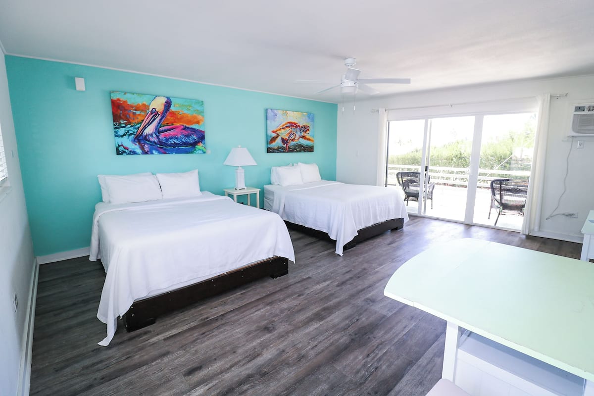 A hotel room with two beds, a ceiling fan, and a view of the outdoors.
