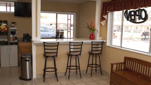 A kitchen area with a window, three bar stools, a trash can, and a wooden bench. - Budget Inn and Suites Colby (Colby)