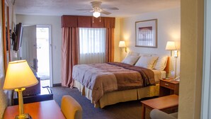 A hotel room with a bed, two bedside lamps, a desk, a chair, a ceiling fan, and a door leading to a balcony. - Budget Inn and Suites Colby (Colby)