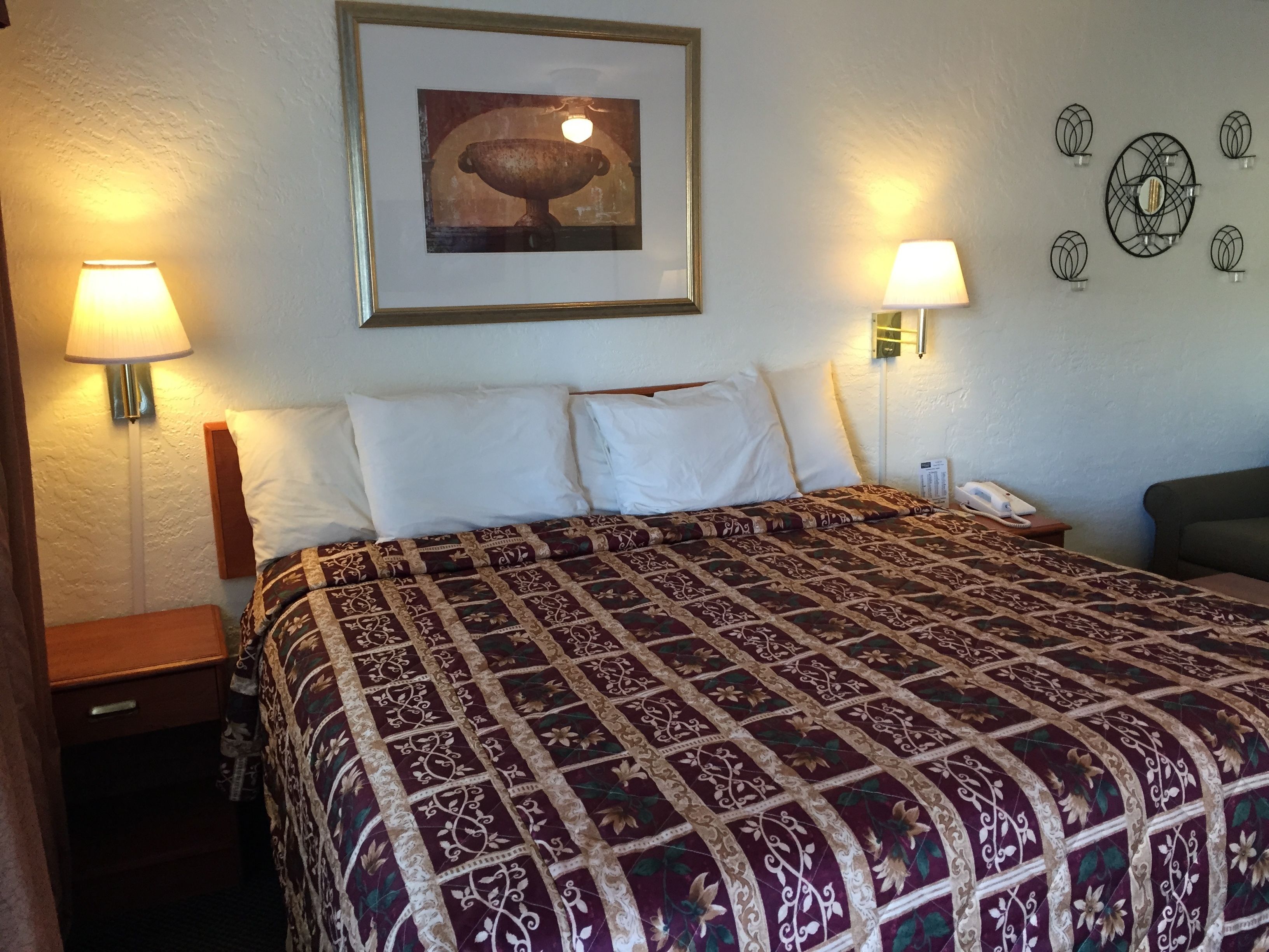 Une chambre d’hôtel avec un grand lit, deux lampes de chevet, un tableau encadré au mur et un téléphone sur la table de chevet.