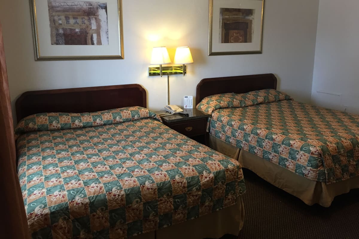 A hotel room with two beds, each with a floral-patterned bedspread, a nightstand with a lamp, and framed artwork on the walls.