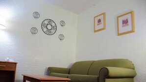A room with a green sofa, a wooden table, and wall decorations including framed pictures and abstract wall art. - Budget Inn and Suites Colby (Colby)