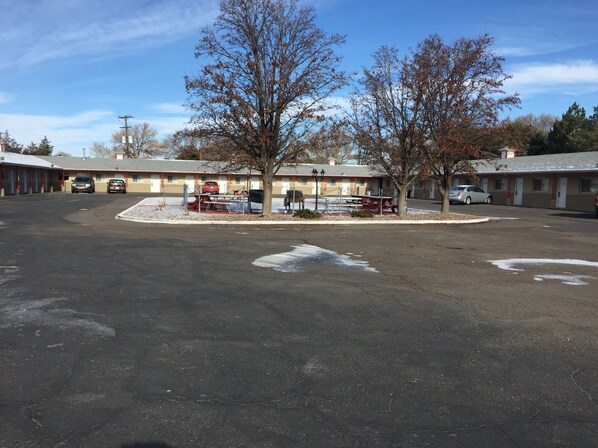 A motel with a parking lot, several cars parked, and a few trees in front of the buildings.