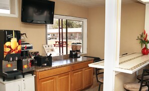 A kitchen with a coffee machine, a fruit juice dispenser, and a window with a view of the outside.