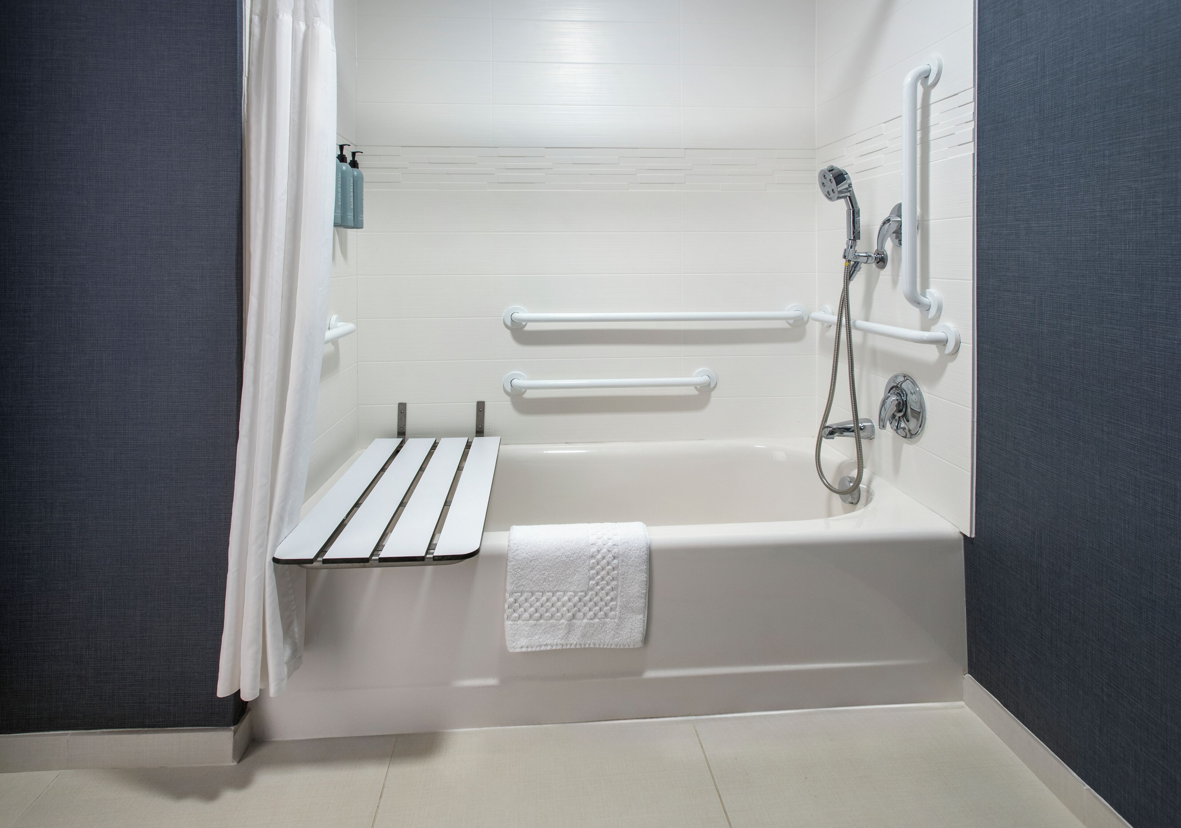 A modern bathroom with a bathtub, grab bars, a towel rack, and a showerhead.