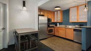 A compact kitchen with wooden cabinets, stainless steel appliances, and a small dining area with stools. - Residence Inn by Marriott Pittsburgh Monroeville/Wilkins (Pittsburgh)