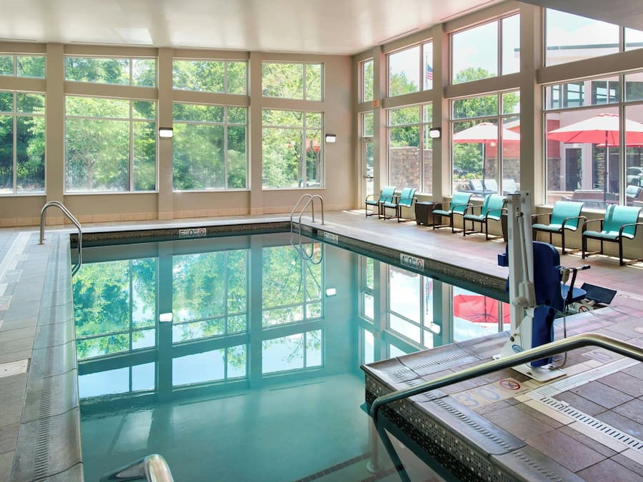 An indoor swimming pool with clear glass walls, a lifeguard chair, and a sunshade outside.