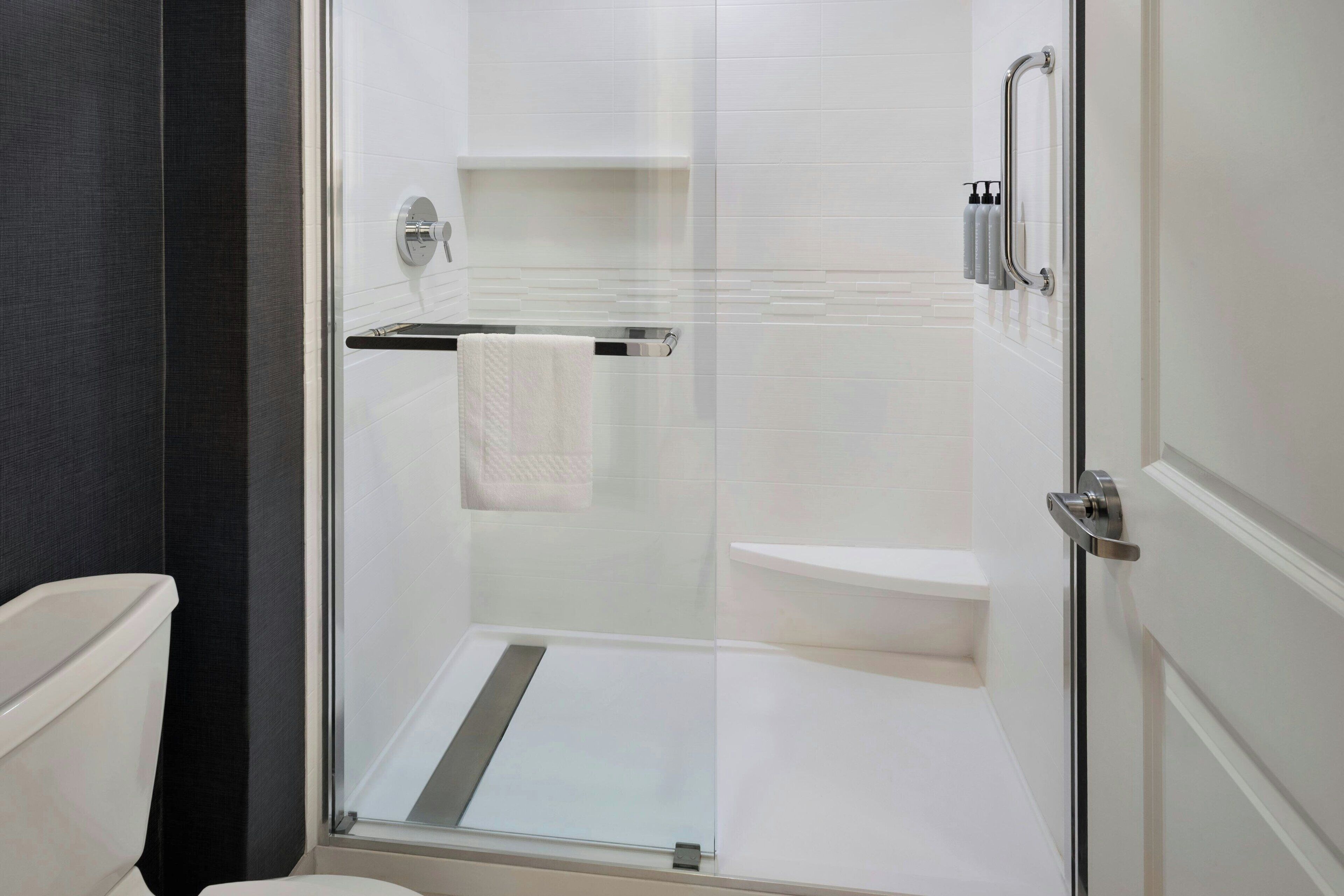 A modern bathroom with a glass shower enclosure, a white toilet, and a towel rack.