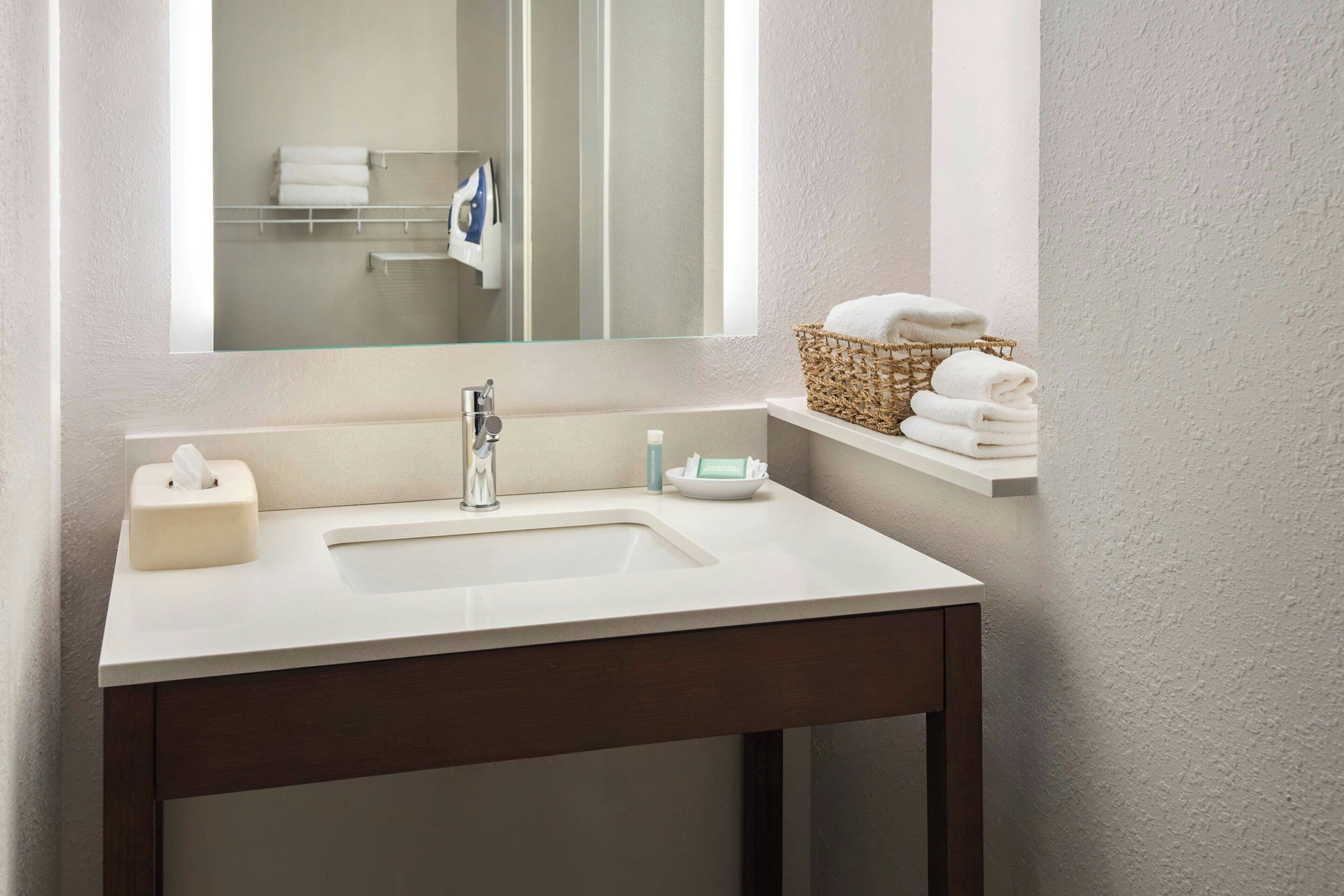 A bathroom with a white sink, a mirror, a towel rack, and a basket of towels.