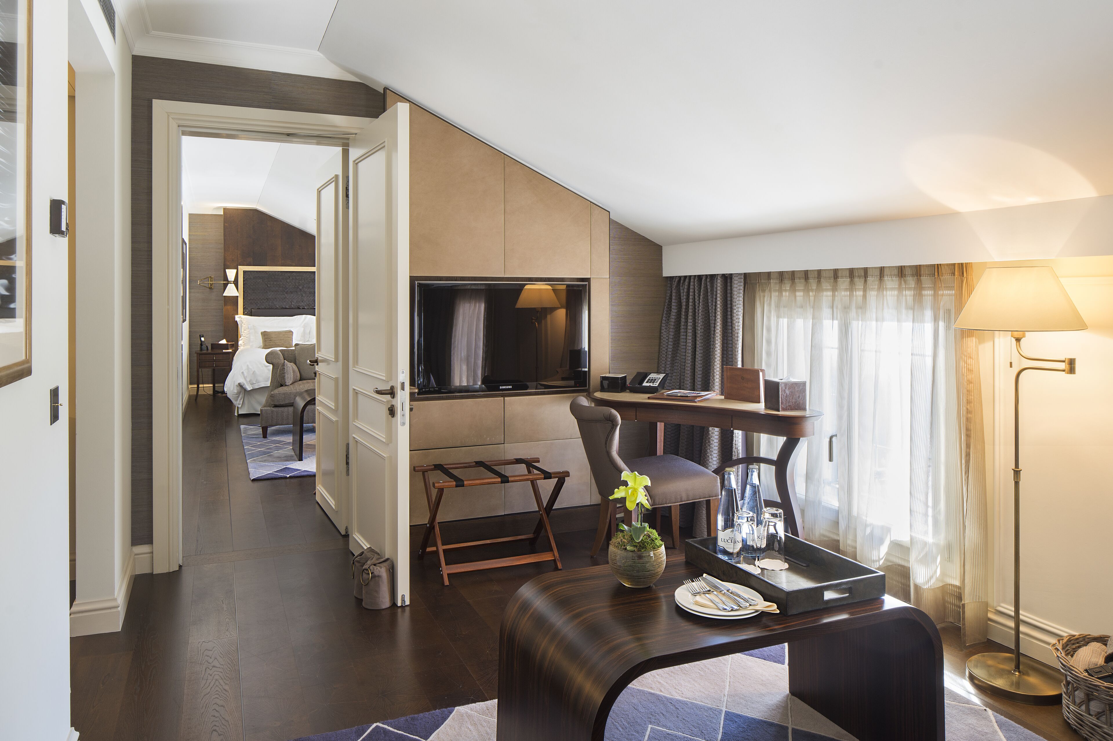 A modern hotel room with a dining area, a TV, and a seating area with a plant.