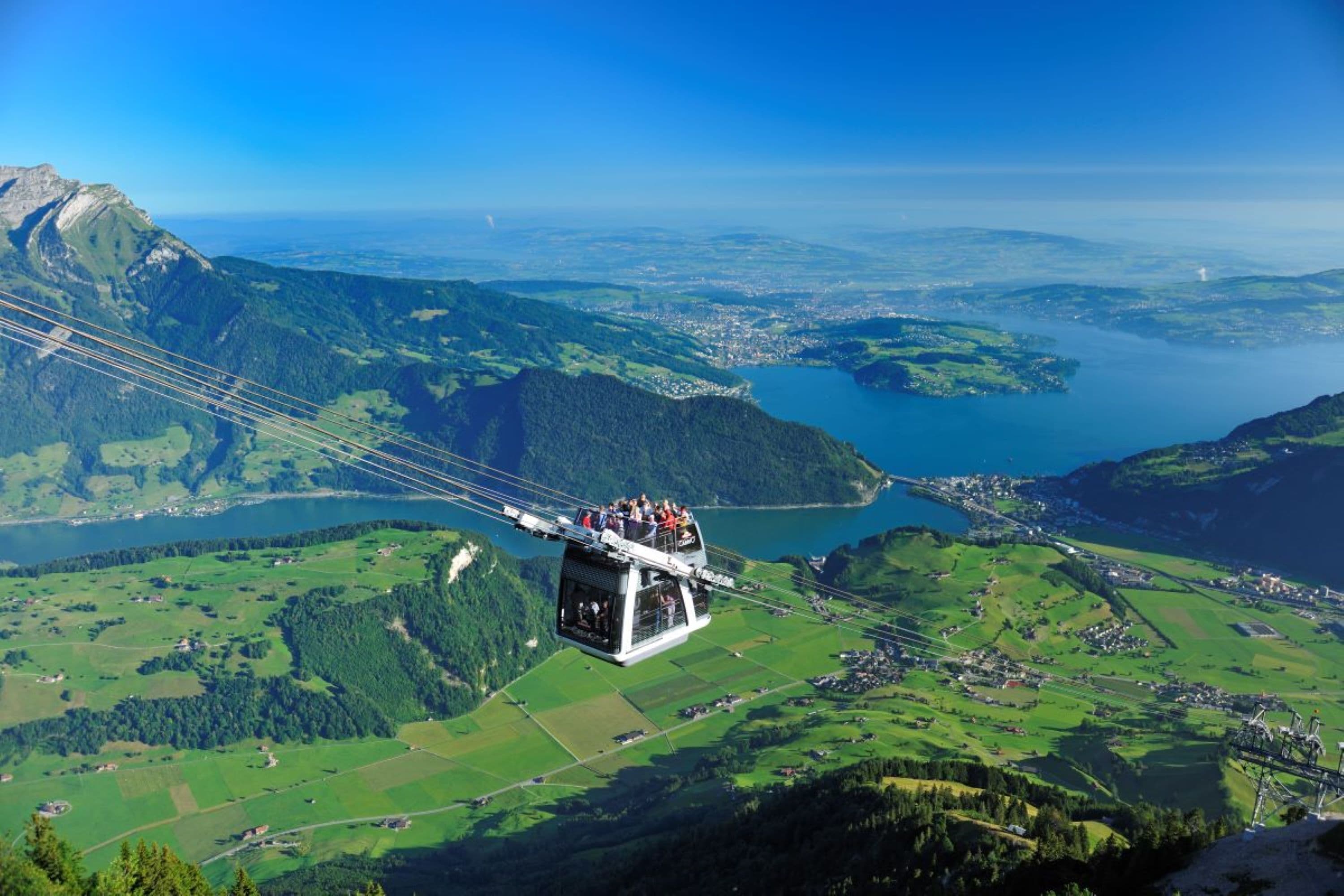 Une télécabine transportant des passagers, survolant un paysage montagneux avec un lac en contrebas.