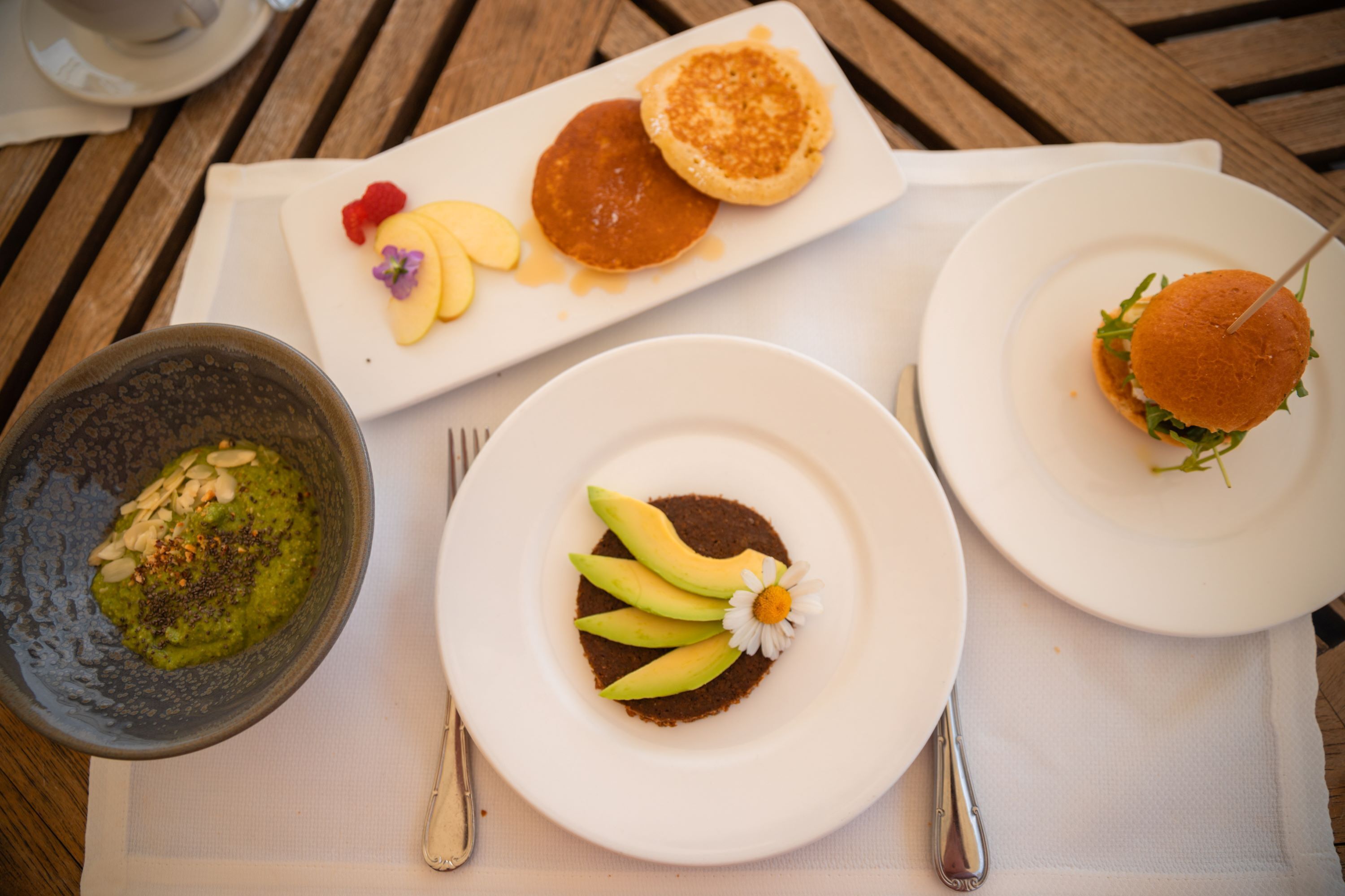 A dining table with three plates of food, a bowl of soup, and a cup.