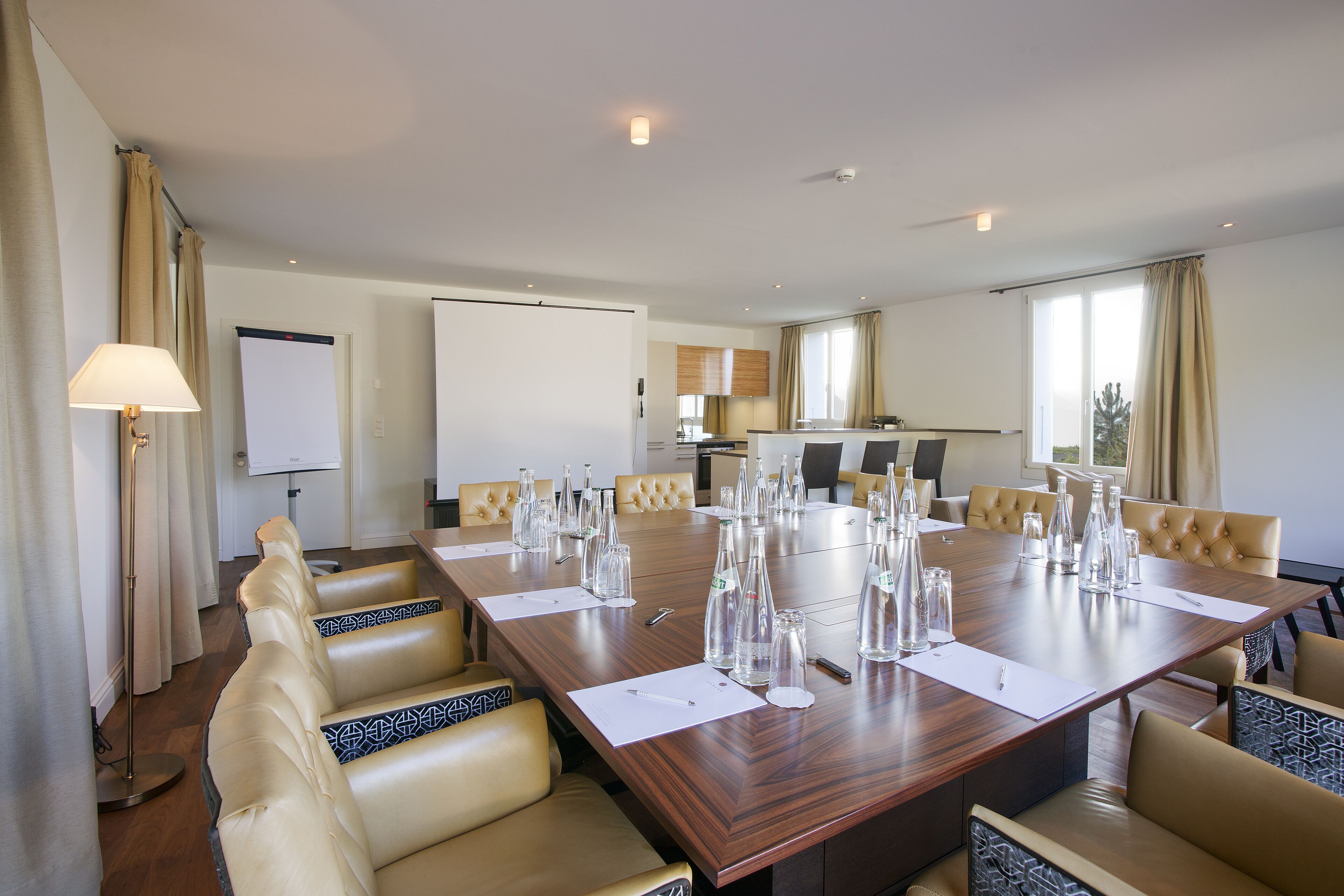 Una sala conferenze con un grande tavolo in legno, poltrone in pelle color beige e uno schermo per proiettore.