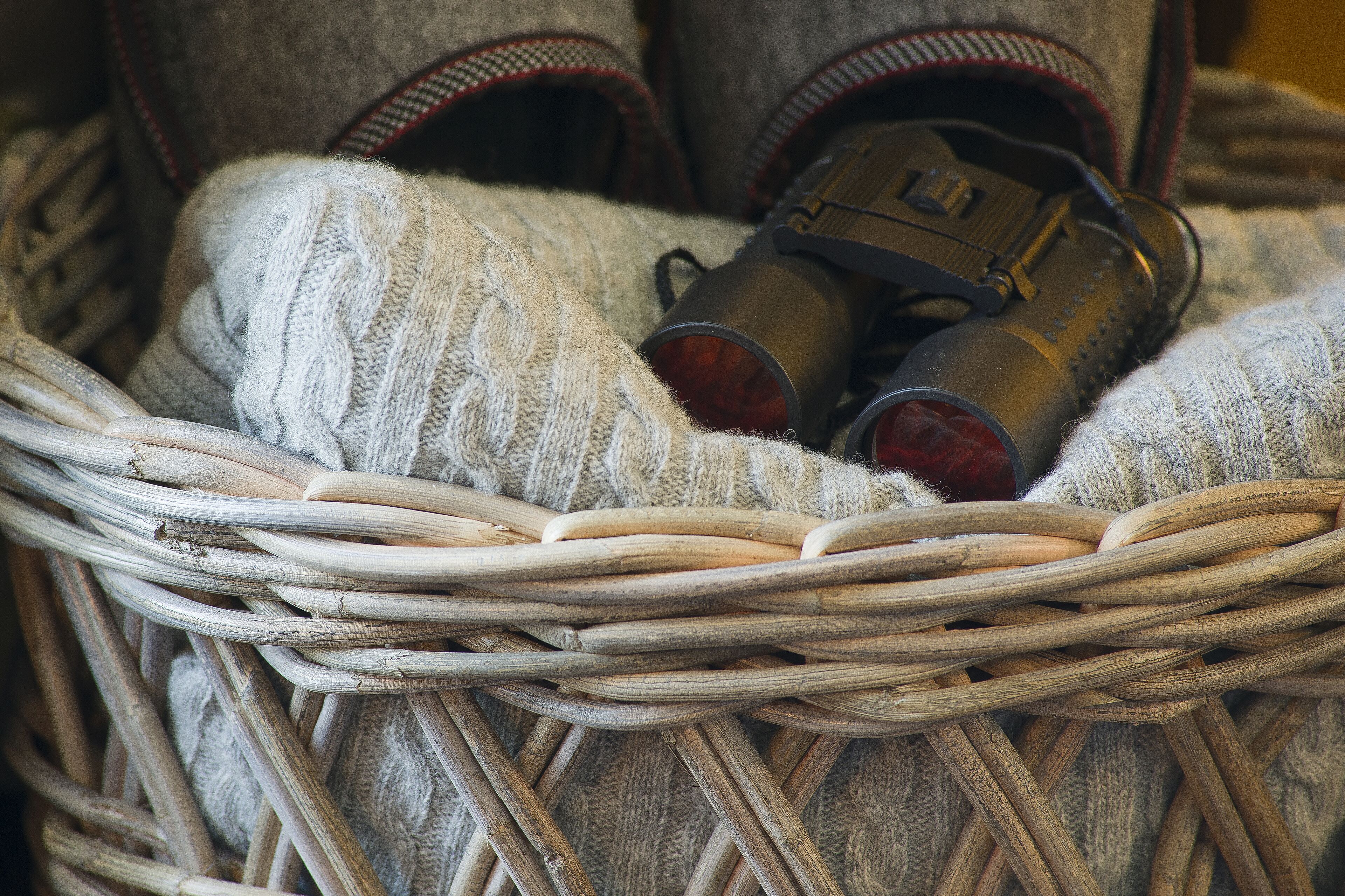 A wicker basket containing a pair of shoes and a metallic object.