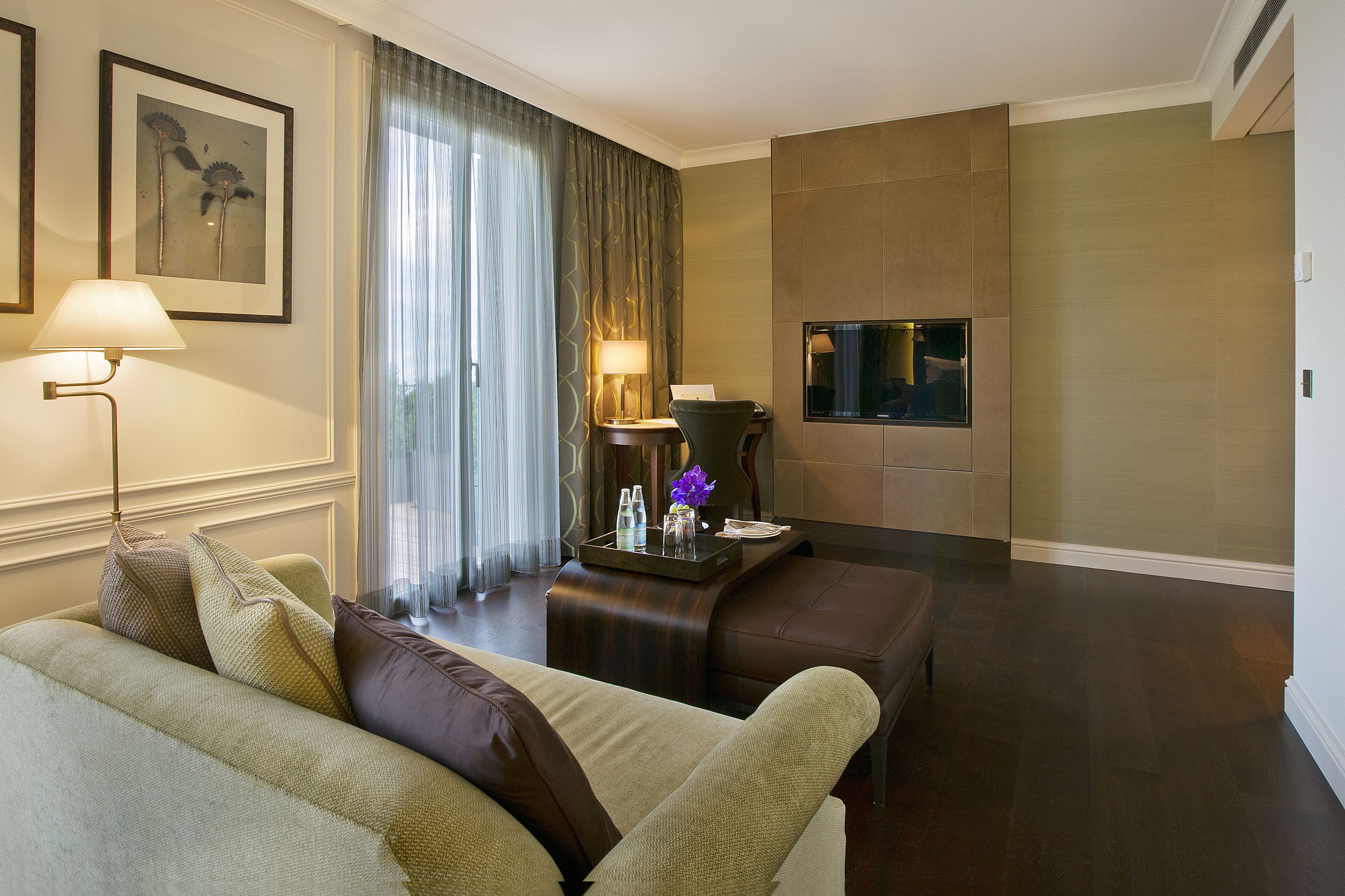 A hotel room with a sofa, a small table with a tray of items, a lamp, and a television.