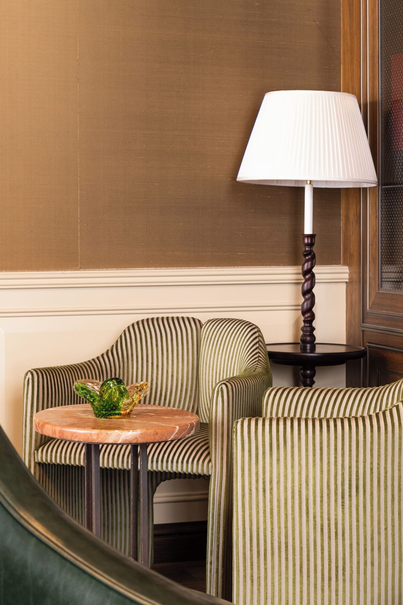A corner seating area with striped upholstered chairs, a small round table with a marble top, and a classic lamp with a twisted base.