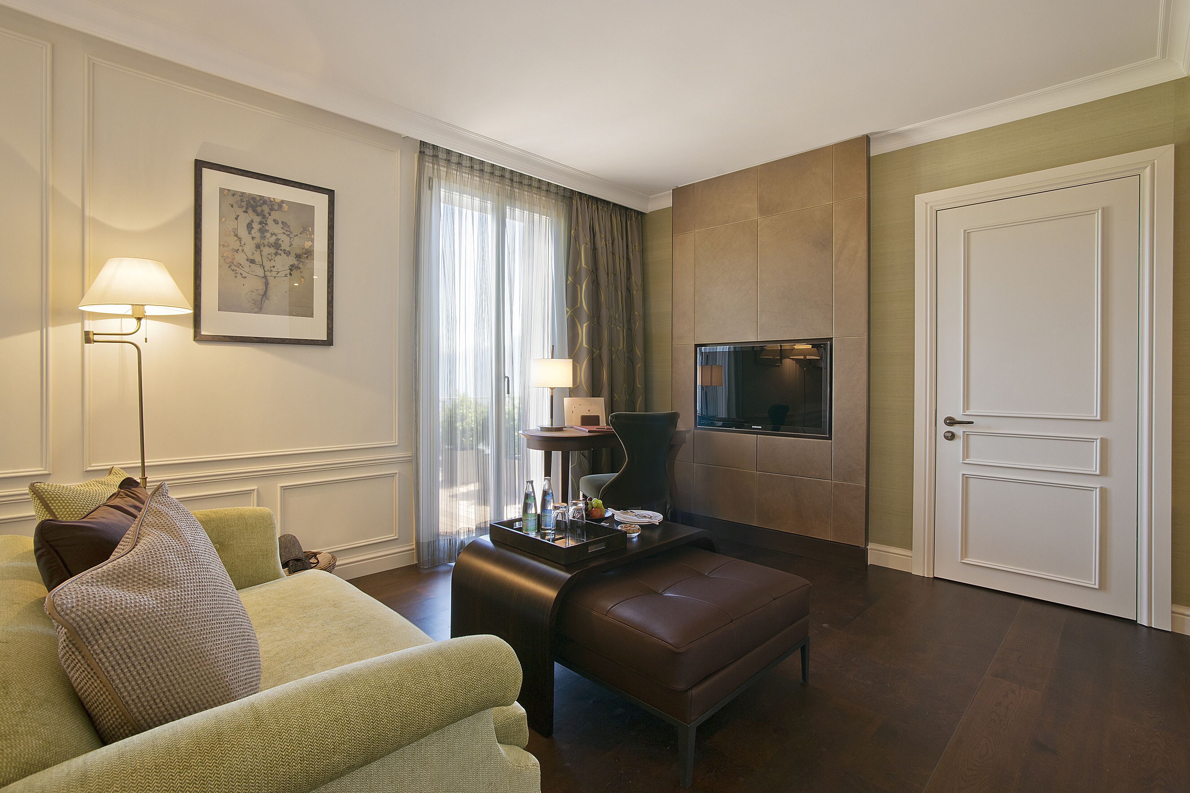 Una habitación de hotel moderna con un sofá, una mesita con lámpara, televisión y una puerta.