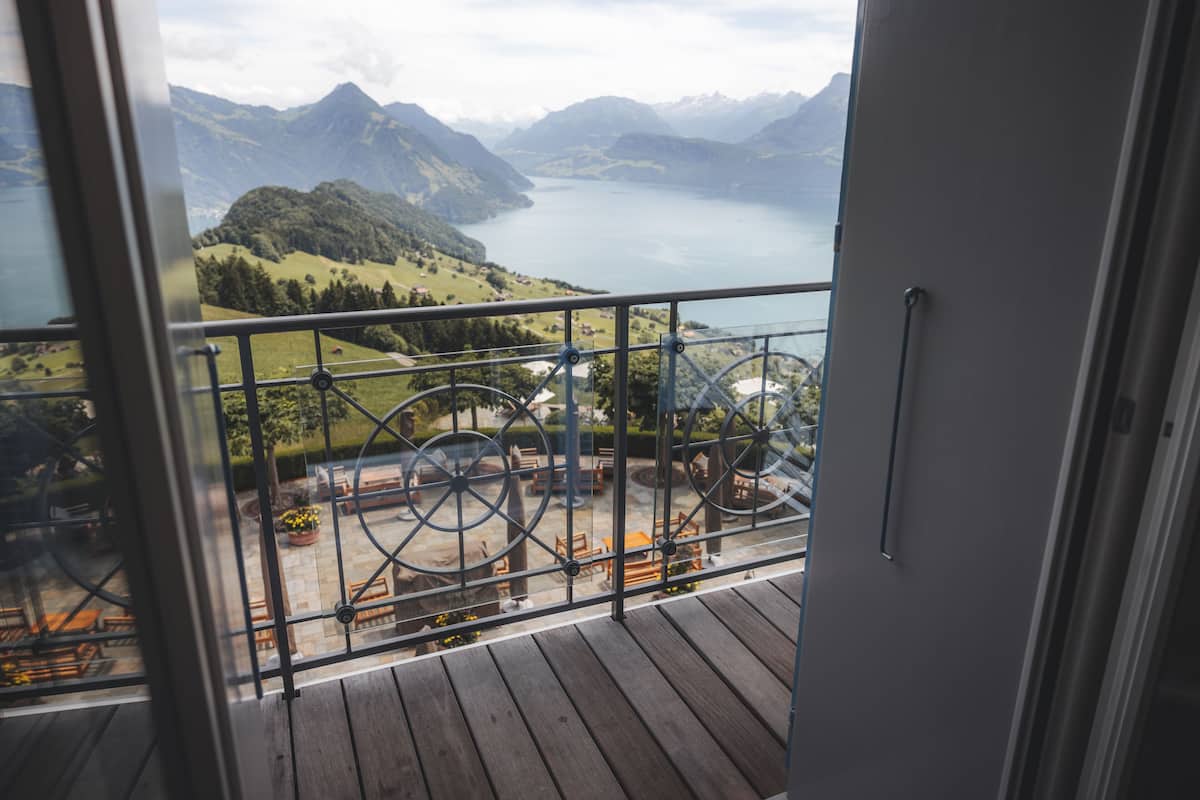 A balcony with a metal railing overlooking a mountainous landscape and a lake.