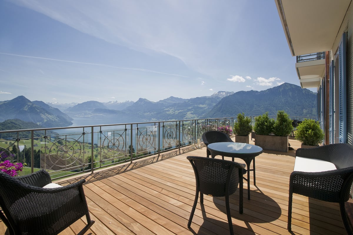 A wooden deck with outdoor furniture, a view of mountains, and a lake.