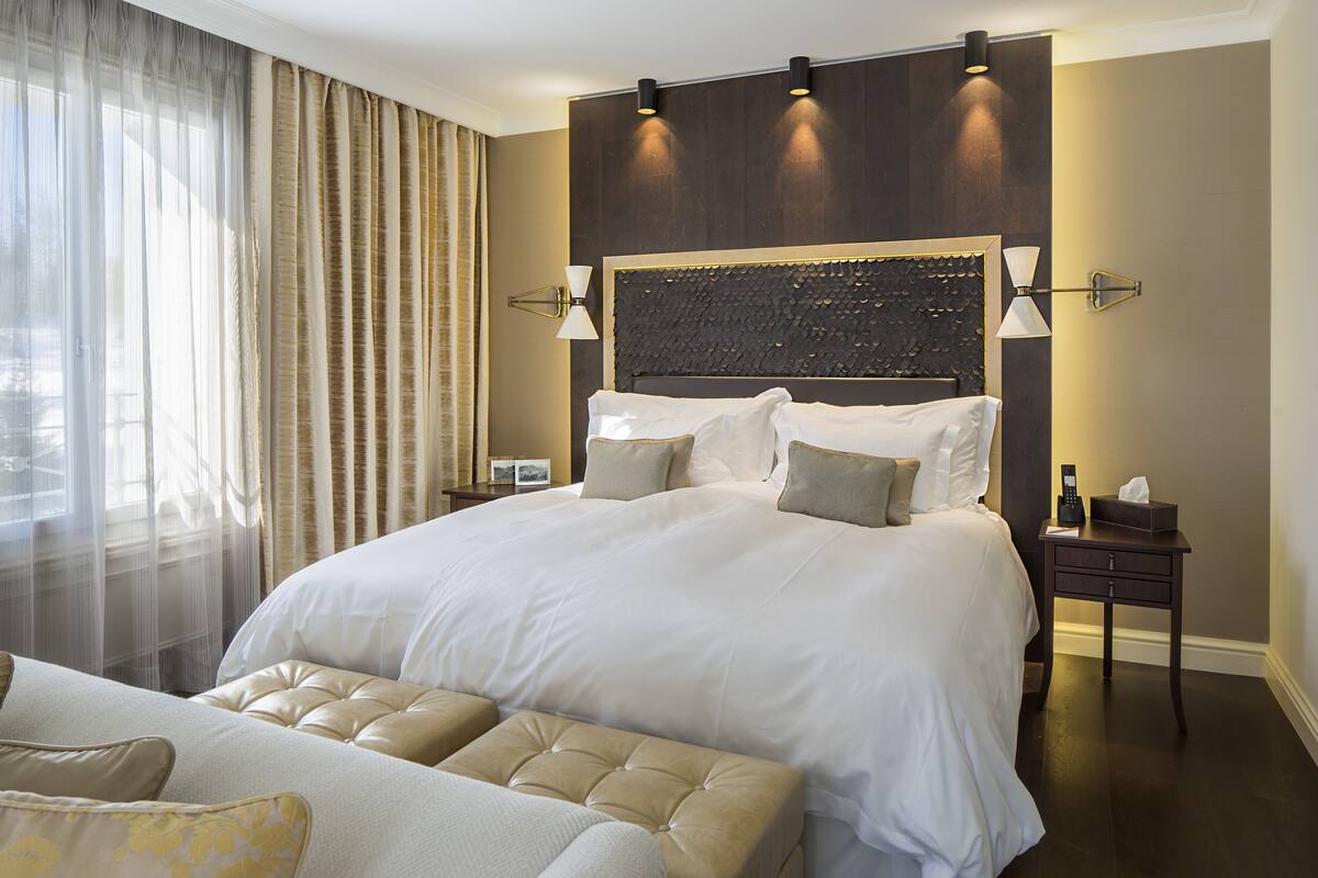 A large bed with a headboard, two bedside tables, a nightstand, and a sofa.