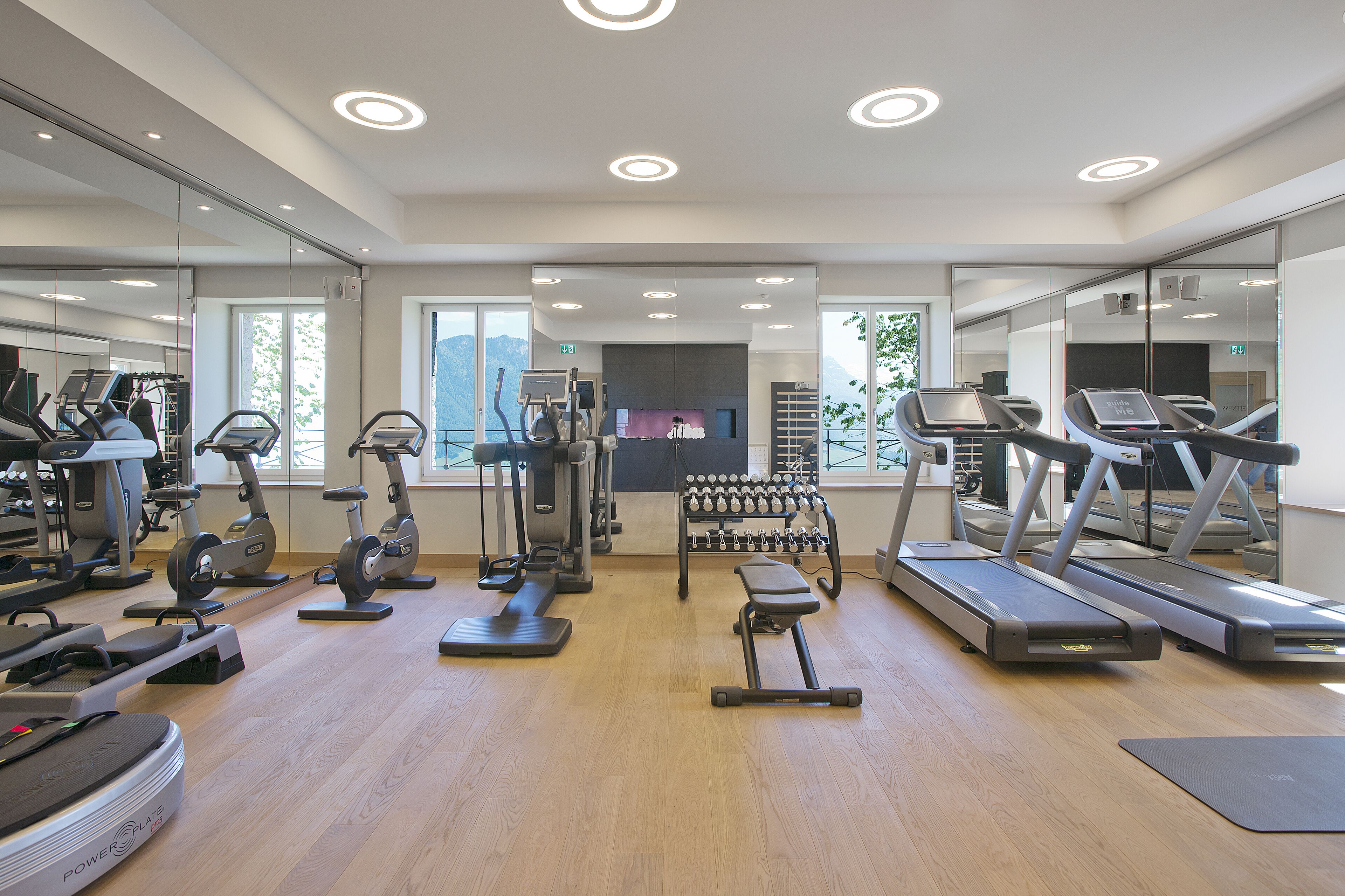 A modern gym with cardio machines, weight stations, and a mirror wall.