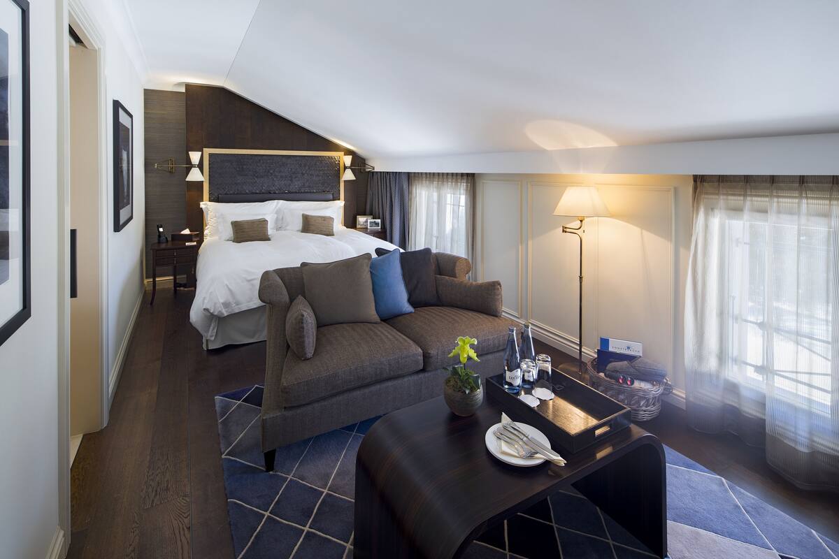 A hotel room with a bed, a sofa, a dining table, and a lamp.