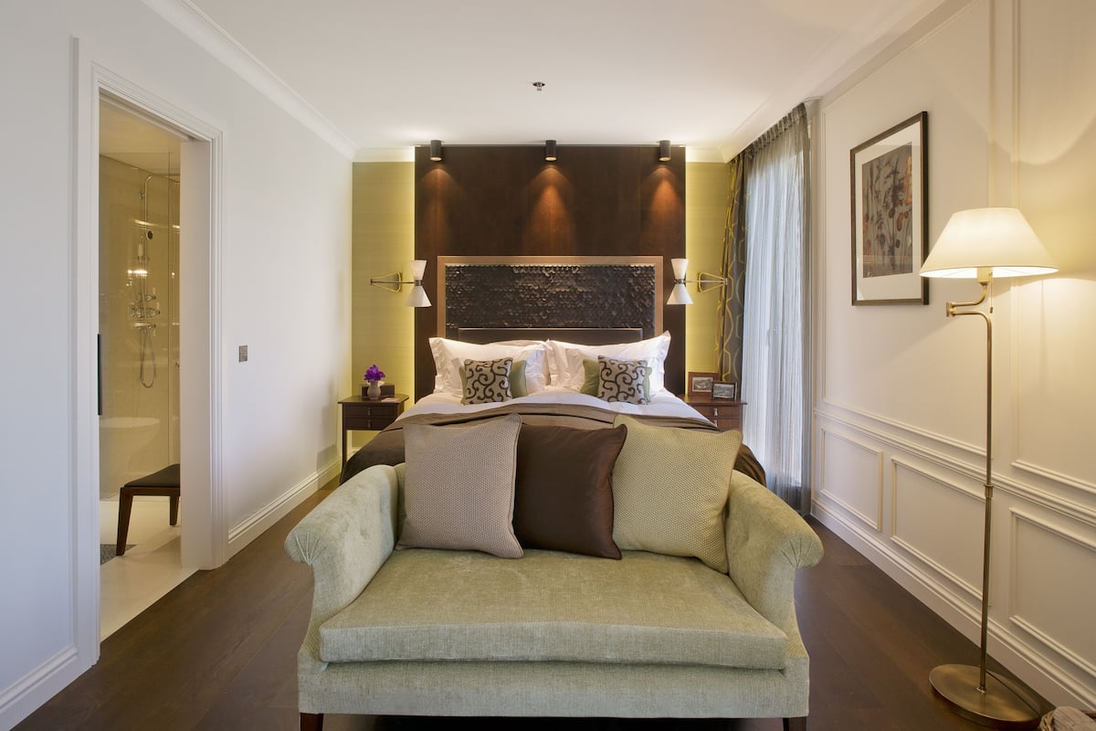 A hotel room with a bed, a sofa, a bedside table, a lamp, and a framed picture on the wall.