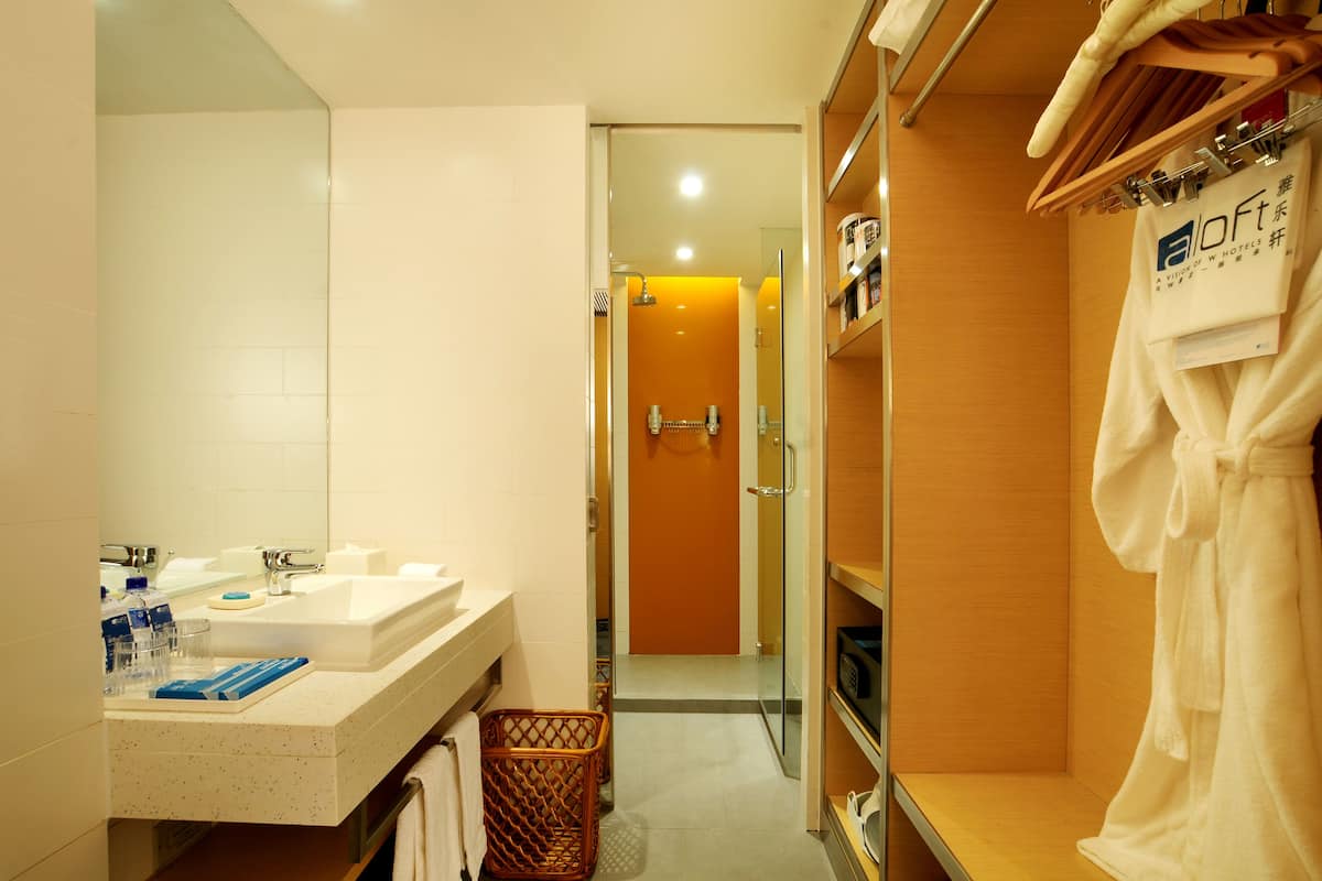 Une salle de bain d’hôtel équipée d’un lavabo, d’un miroir et d’étagères où sont rangés les articles de toilette.