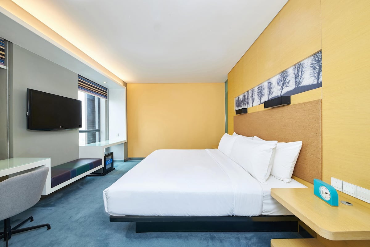 Een hotelkamer met een bed, een bureau, een televisie en een kunstwerk aan de muur.