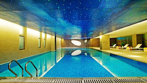 An indoor swimming pool with a blue tiled floor, a ceiling with star-like lights, and lounge chairs on the right side. - Aloft Zhengzhou Shangjie (Zhengzhou)