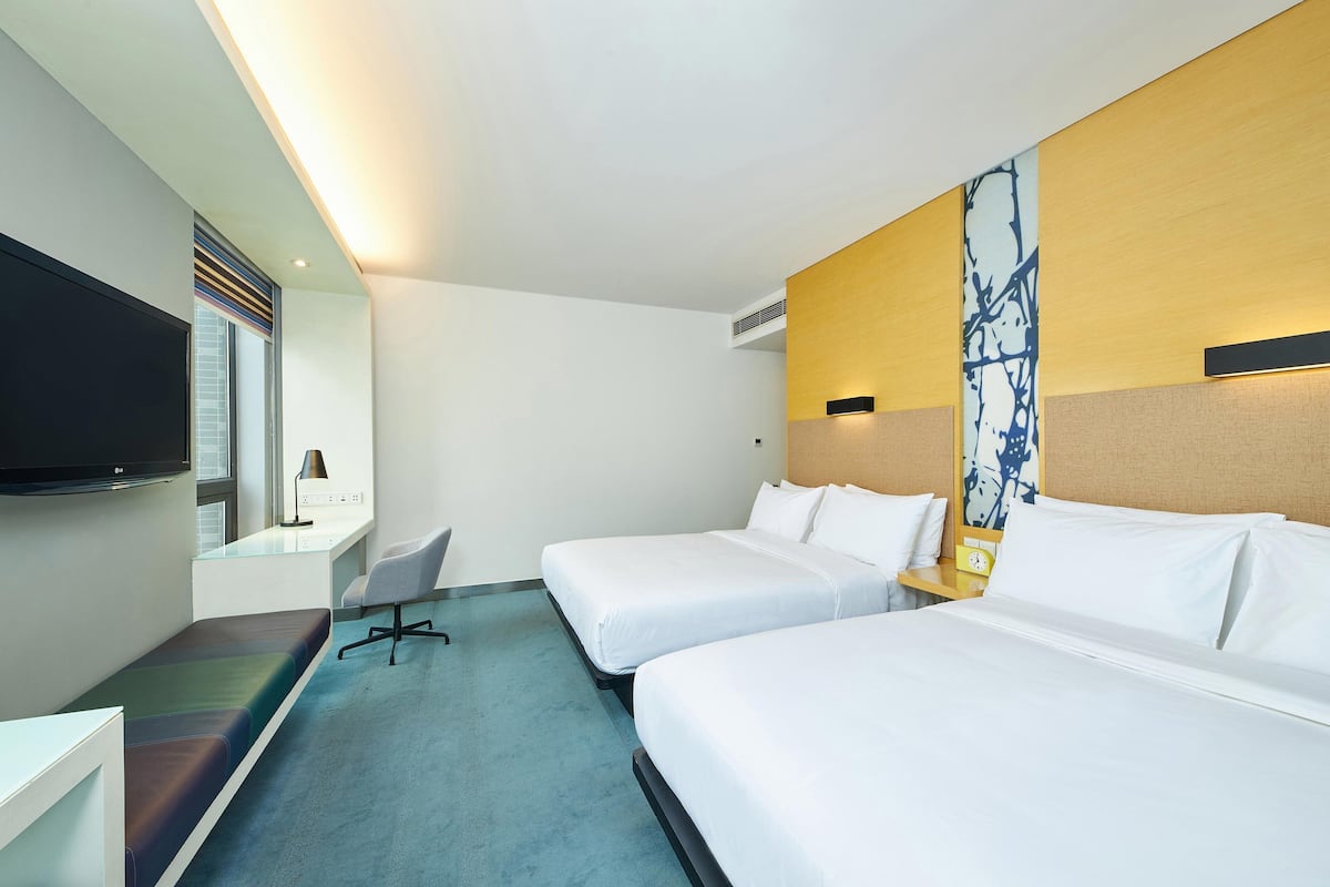 Een hotelkamer met twee bedden, een bureau met stoel, een flatscreen televisie en een groot raam.