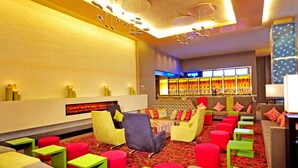 A modern lounge area with colorful seating, a bar in the background, and a patterned carpet. - Aloft Zhengzhou Shangjie (Zhengzhou)
