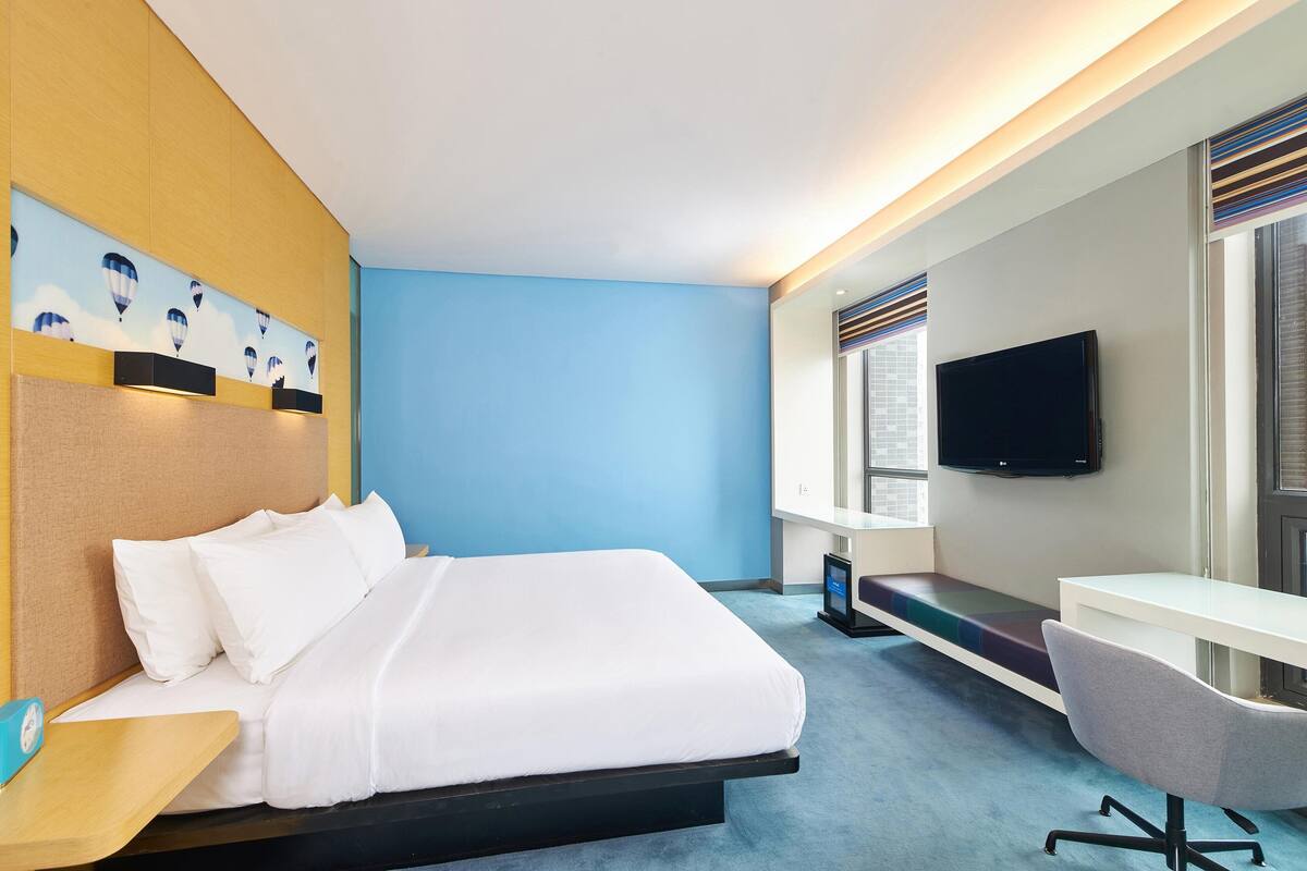 Een hotelkamer met een bed, een bureau, een stoel, een televisie en een kunstwerk aan de muur.
