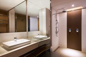 A modern bathroom with two sinks, a large mirror, and a shower area.