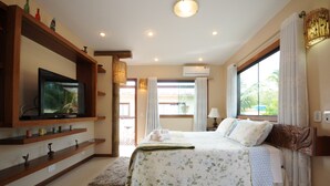 Ein Schlafzimmer mit einem Bett, einem an einer Holzwand montierten Fernseher, einem Fenster mit Vorhängen und einer Klimaanlage.