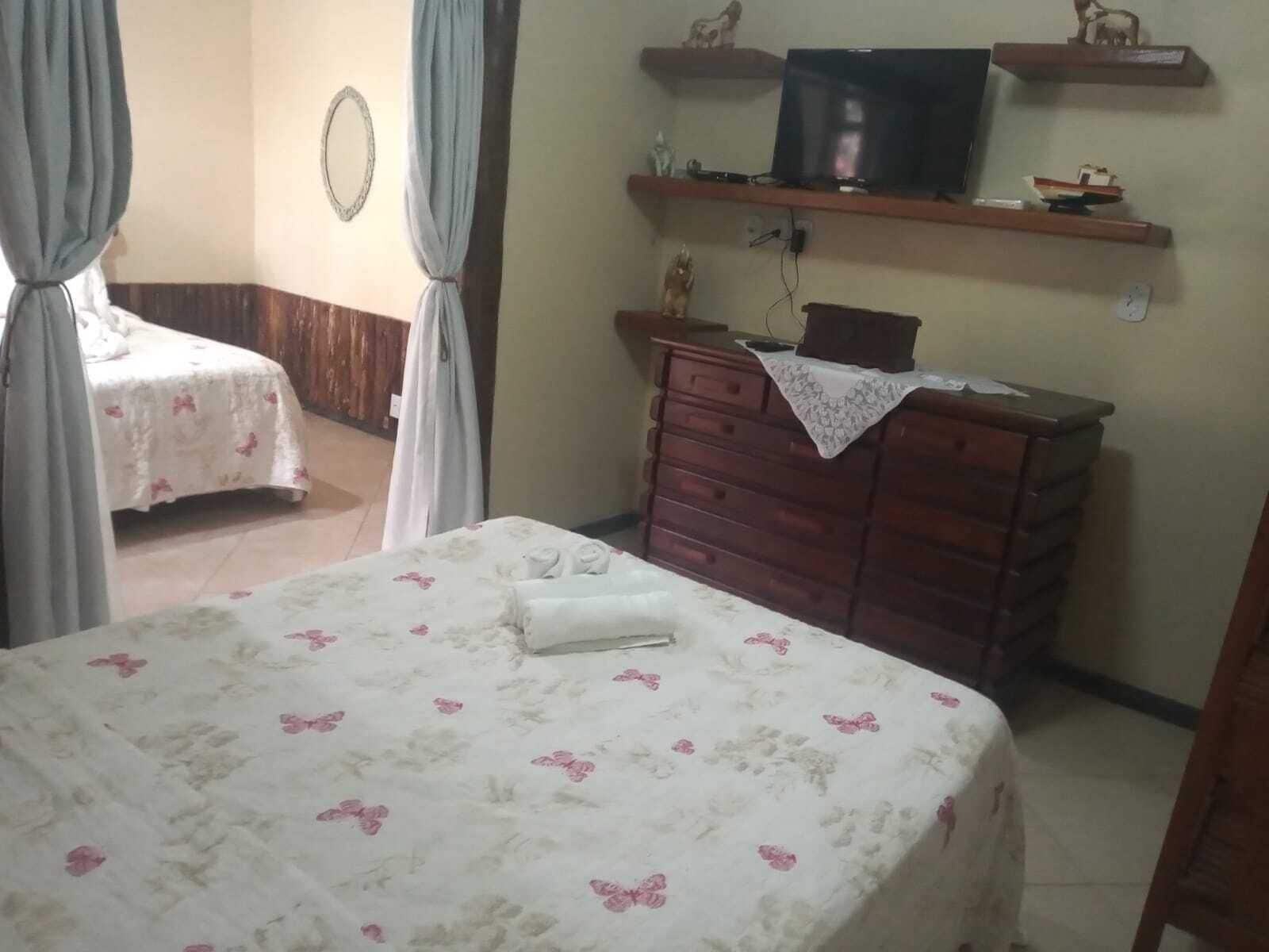 Une chambre à coucher avec un lit, une commode, un téléviseur posé sur une étagère et une petite table.