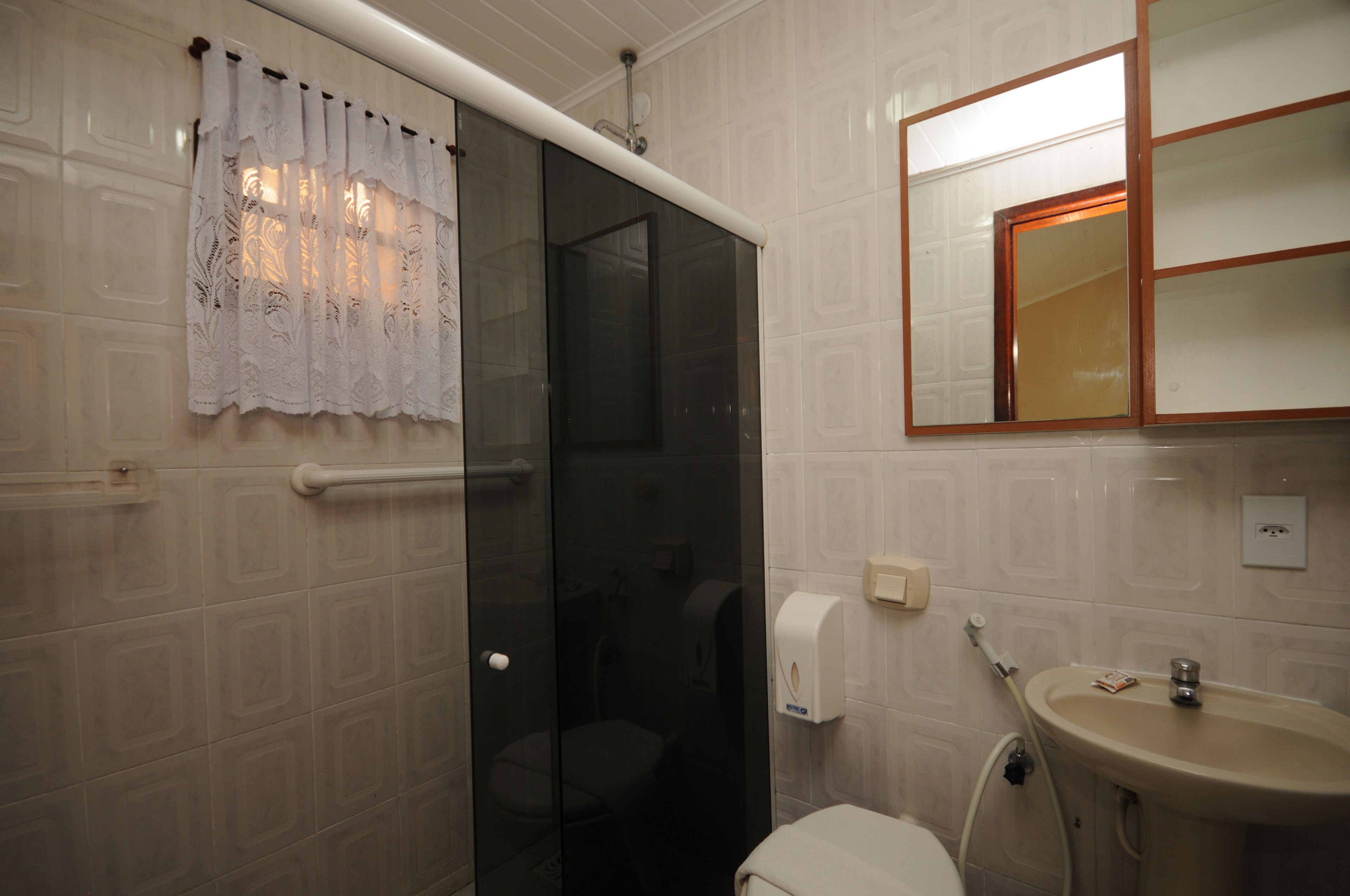 Un baño con cabina de ducha de vidrio, inodoro, lavamanos y espejo con marco de madera.